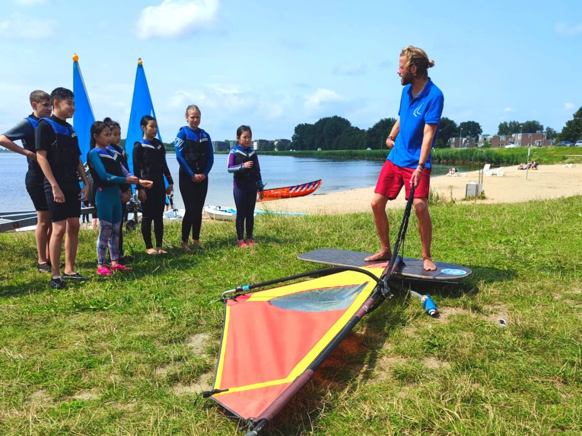 Instructeur legt de windsurfles uit aan een groep kinderen